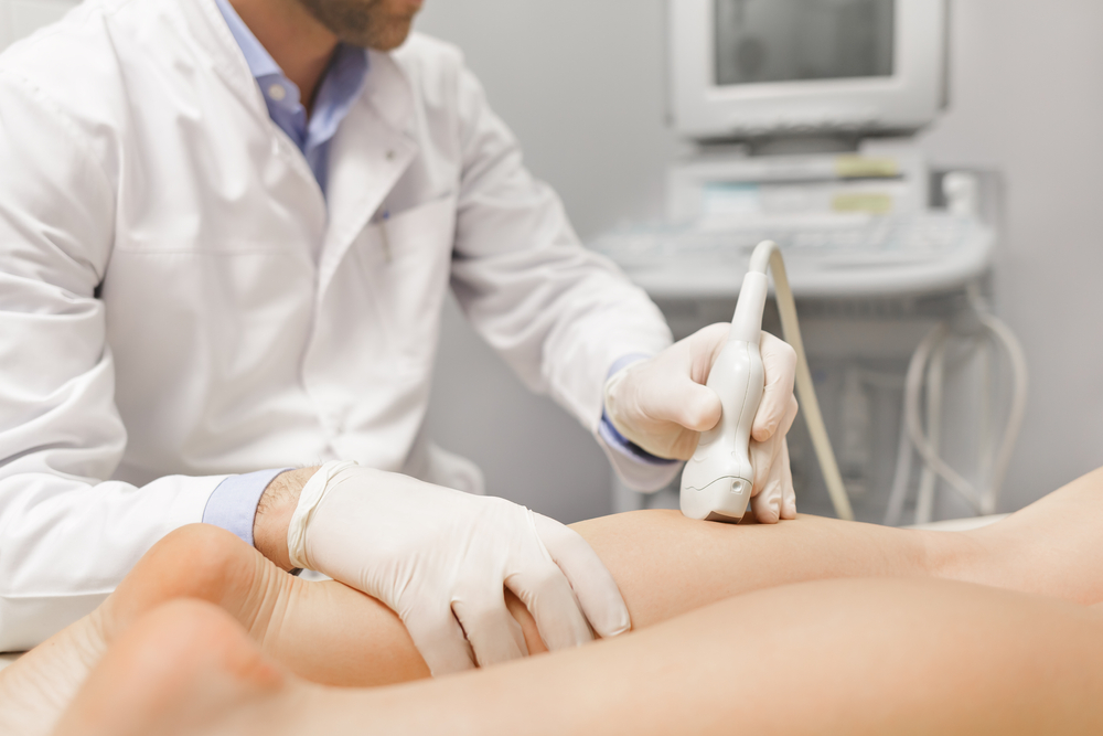 A doctor using an ultrasound to check circulation in a patient's legs.
